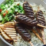 Lamb kofta skewers on a platter with pita and rice.