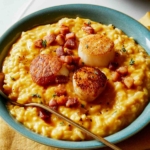 Pumpkin risotto with seared scallops on top in a bowl with a spoon in it.