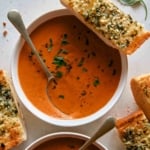 Tomato soup recipe in two bowls with garlic bread on the side.
