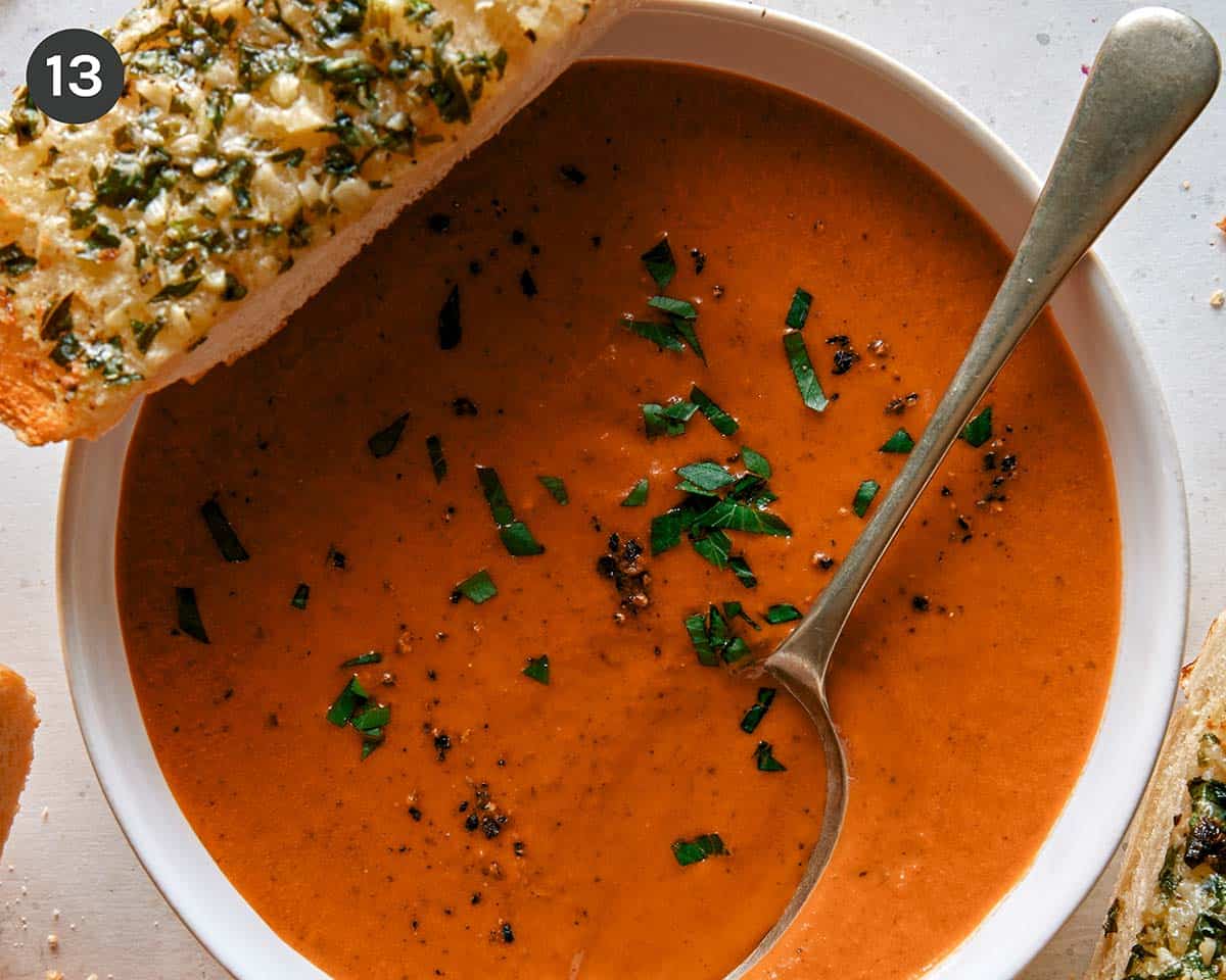 Tomato soup recipe in two bowls with garlic bread on the side.